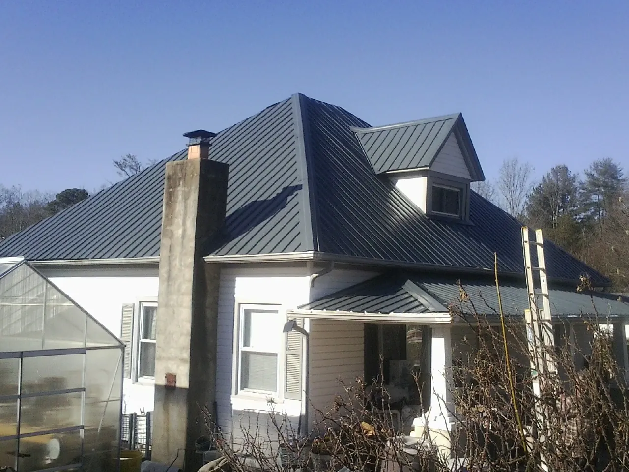 Dark blue standing seam metal roof on a white farmhouse with dormer — Slate & Tile Roof Repair by Roofing Brothers in Conover
